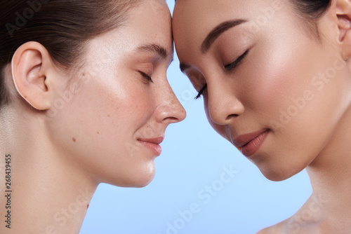 Close up of two interracial attractive women situating against blue background