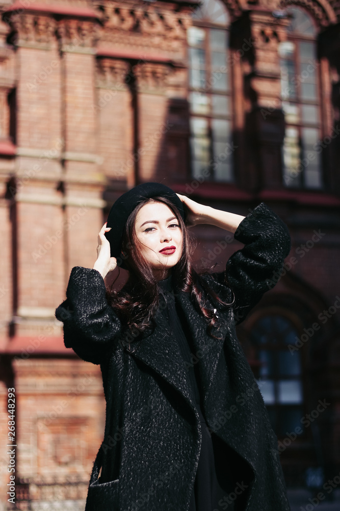 Naklejka premium A girl in a black coat walks down the street