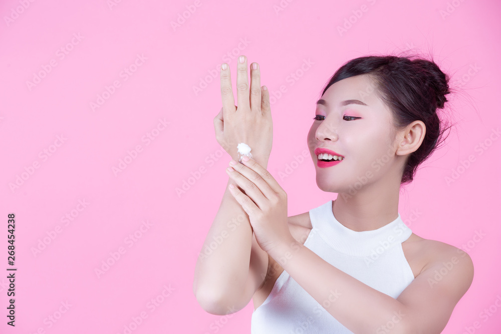 ..Beautiful Asian woman holding a bottle of product on a pink background...