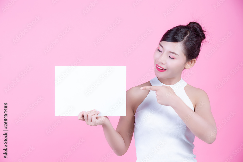 Beautiful woman holding a white board sheet on a pink background. Beautiful woman holding a white board sheet on a pink background.