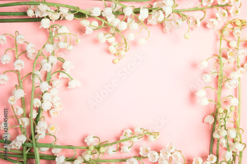 Frame of lily of the valley flowers on a pink background.