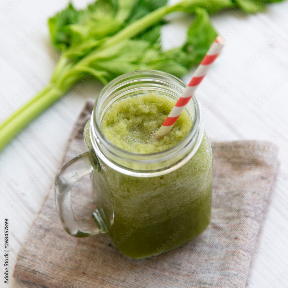 Glass jar of green celery smoothie on a white wooden surface, low angle view. Close-up. Glass jar of green celery smoothie on a white wooden surface, low angle view. Close-up.