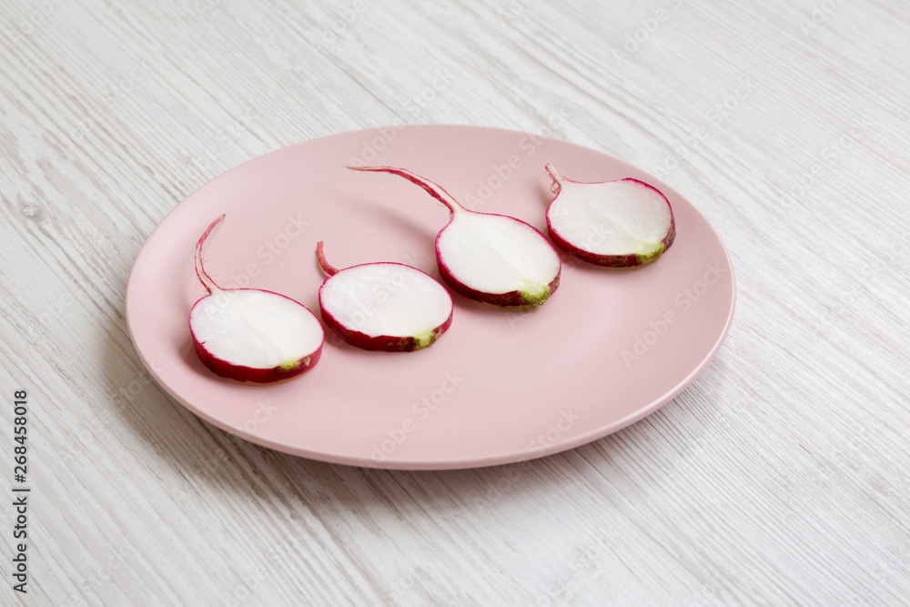 Radish slices on a pink plate over white wooden background, side view. Close-up. Radish slices on a pink plate over white wooden background, side view. Close-up.