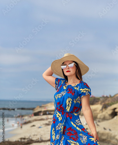 Beautiful Female Standing at the Cove Wearing Sunglasses a Summer Hat and a Blue Floral Dress