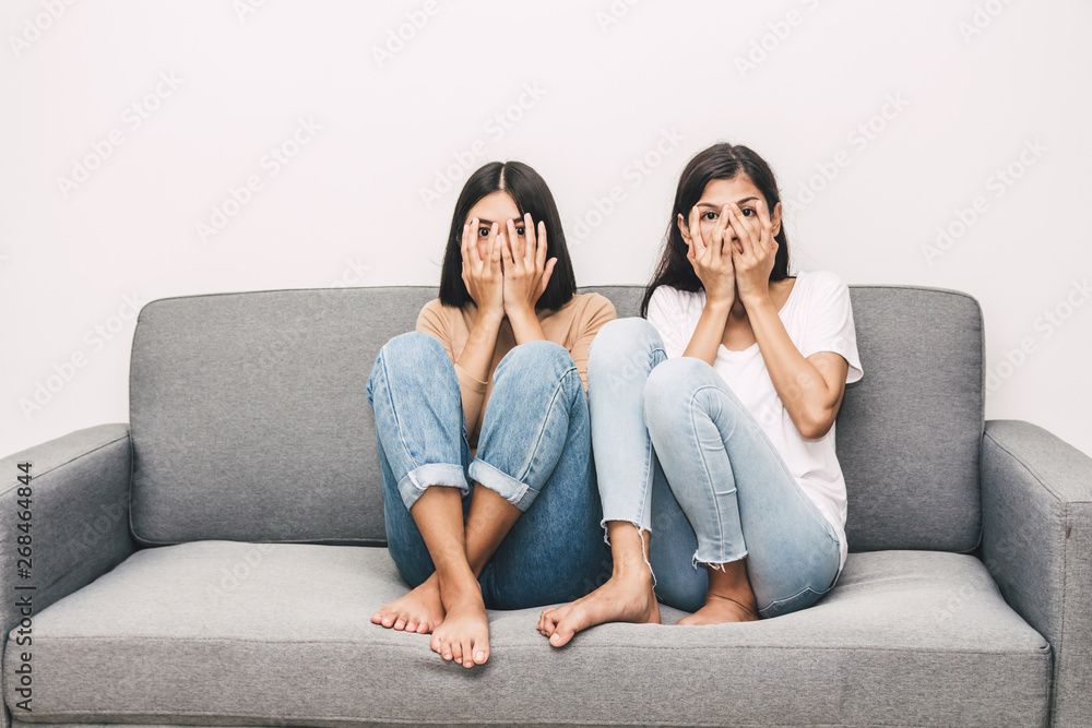 Two scared women on couch watching horror movie on TV at home Two scared women on couch watching horror movie on TV at home