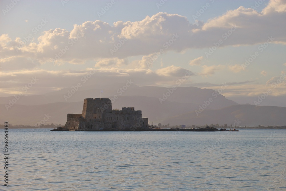 Shortly before sunset in the bay of Nafplio, Peloponnese, Greece. Bourtzi castle and mountain landscape in pastel colors. South-east Europe. Shortly before sunset in the bay of Nafplio, Peloponnese, Greece. Bourtzi castle and mountain landscape in pastel colors. South-east Europe.