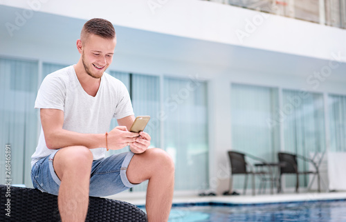 Young man using smartphone near the swimming pool.