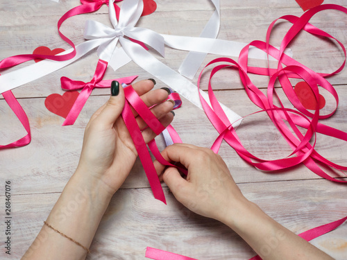 Young woman ties bows from pink satin ribbon on a wooden background. Scrapbooking theme