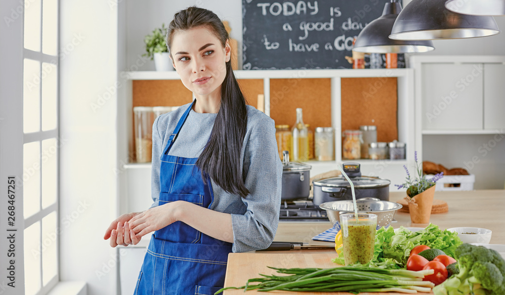 Happy young woman in kitchen with fresh vegetables on the table Happy young woman in kitchen with fresh vegetables on the table