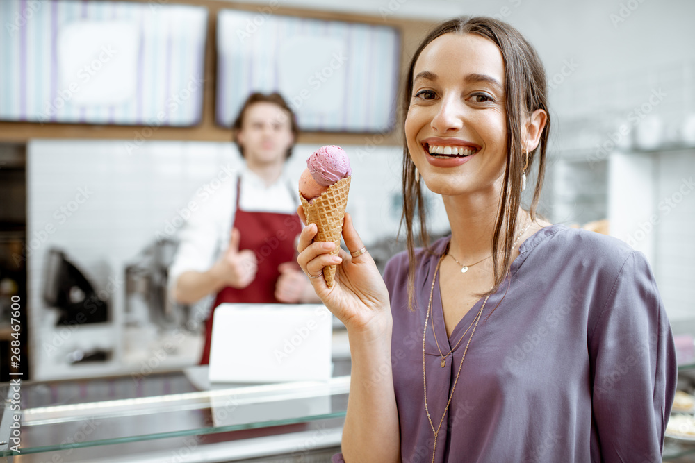Portrait of a young and happpy woman buying ice cream in the pastry shop with salesman on the background Portrait of a young and happpy woman buying ice cream in the pastry shop with salesman on the background