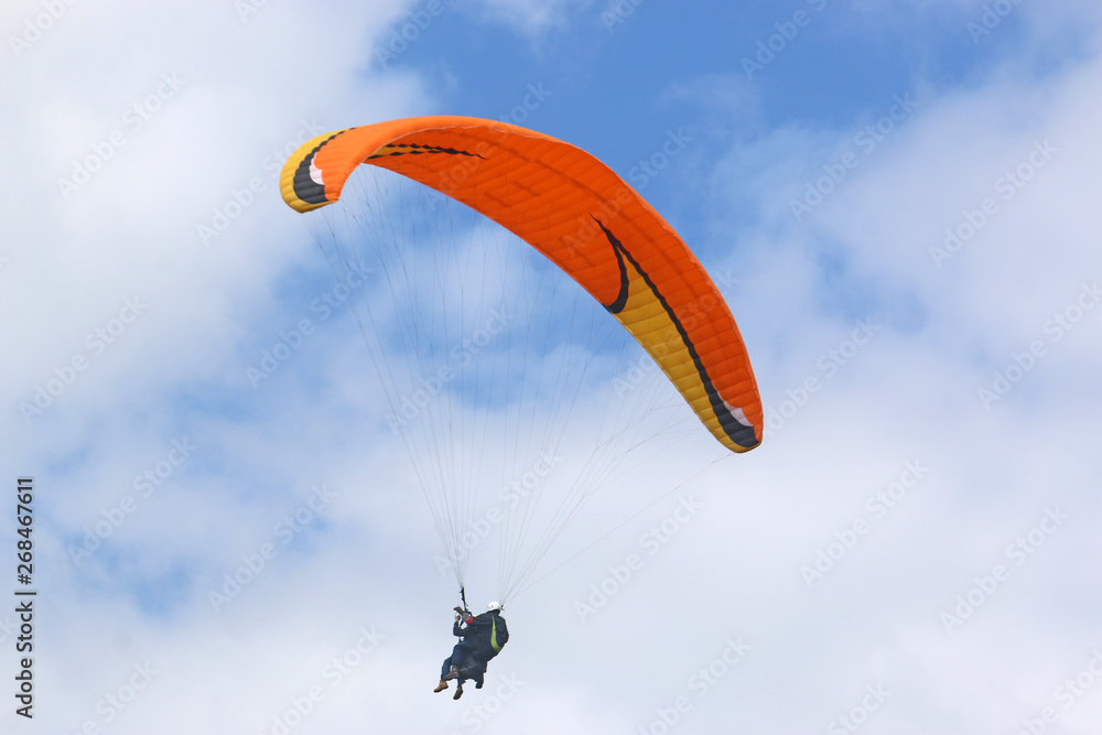Tandem paraglider flying orange wing