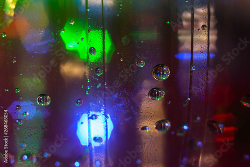 Macro photo of water droplets on a transparent surface in the backlight of multi-colored blurred lights. Abstract textural photo for background. Texture of water droplets in bright light for design.