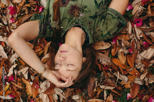 Beautiful female face  young woman traveller lying on coloured leaves in jungle forest