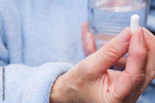woman with pills or capsules on hand and a glass of water