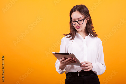 Pretty teenage girl holding and reading on a tablet over yellow background