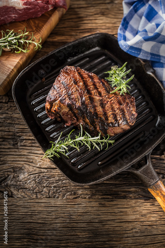 Grilled beef steak in grill pan with herbs rosemary on wooden table