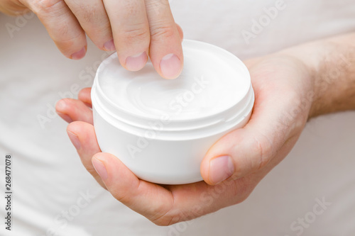 Young, perfect man hands holding white jar and using moisturizing cream. Care about nails and clean, soft, smooth body skin. Front view. Closeup. 