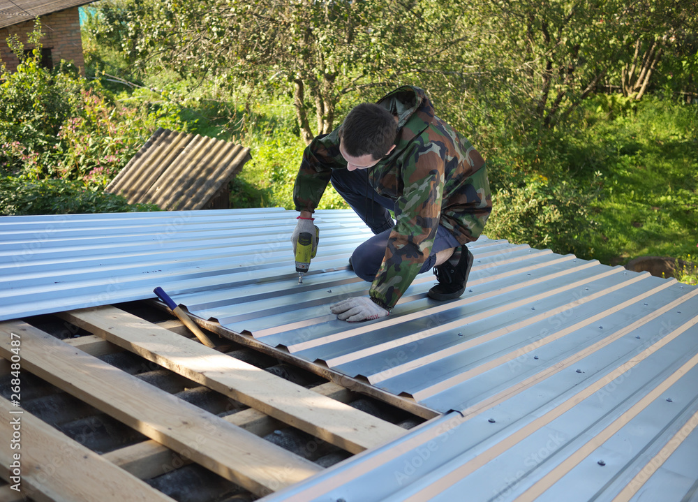 young caucasian man repairing the roof of a home; A worker replaces metal slate on the roof of a home