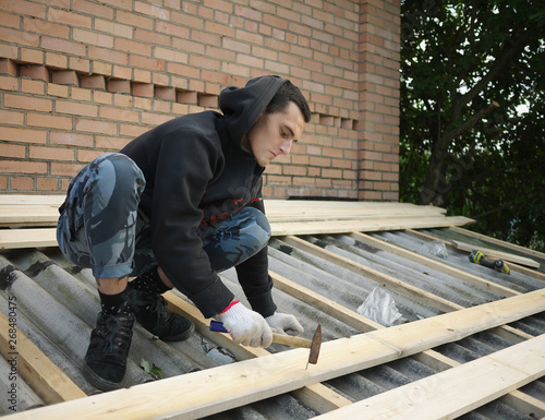 young caucasian man repairing the roof of a home  A worker replaces metal slate on the roof of a home © Dmitry