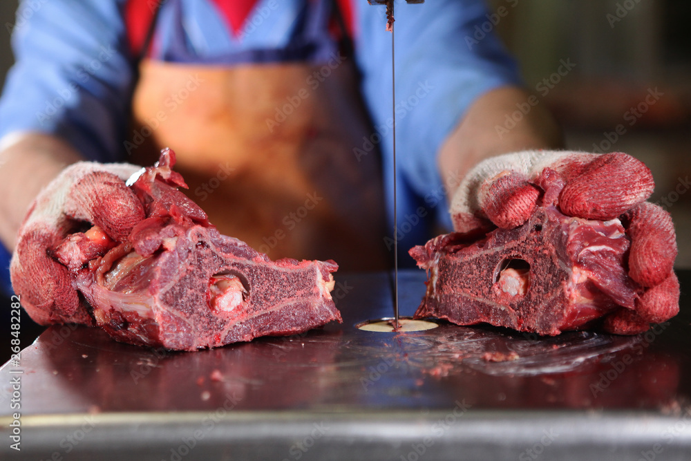 A slaughterhouse worker cuts chunks of meat into portions. Macro photo of a raw piece of meat. Hands out of focus. Professional equipment for cutting meat. Persons employee is not visible.