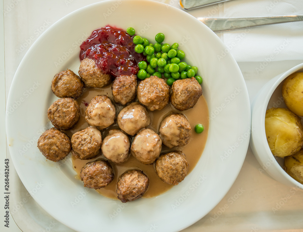 A plate with meat balls, peas, lingonberry jam and potatoes.