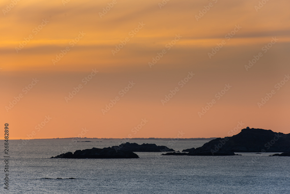 Warm and orange sunset over islands and a coastline far in the horizon.