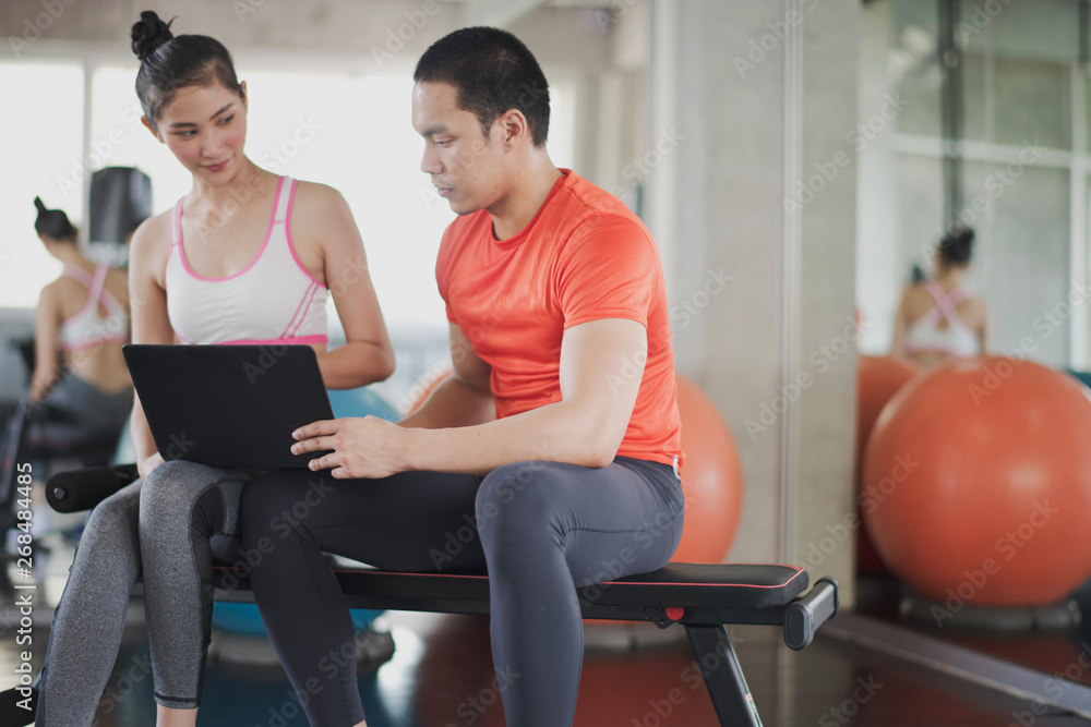 Obraz premium Sport women and men fitness trainer are discussing. Young Asian female talking with coach during workout with at gym. Female coach explaining with laptop computer.