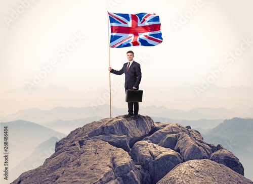 Successful businessman on the top of a mountain holding victory flag 