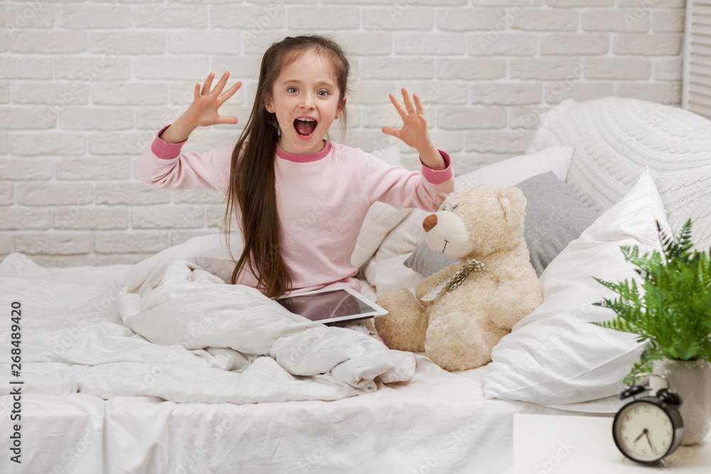 surprised little child girl lies in bed uses digital tablet. child playing on tablet pc. surprised little child girl lies in bed uses digital tablet. child playing on tablet pc.