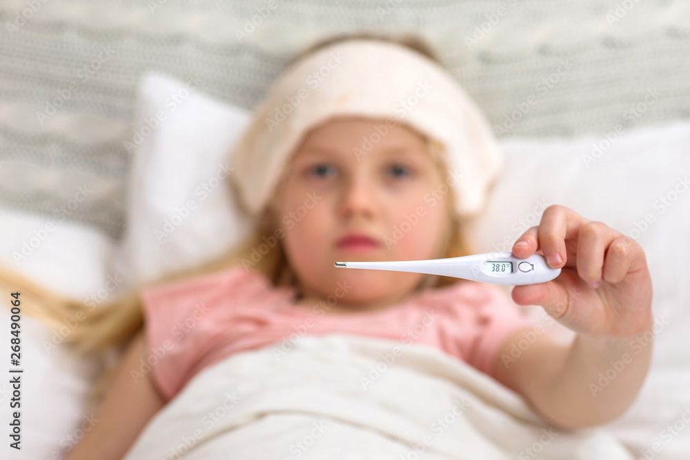 Sick little child girl lying in bed with thermometer. child shows a thermometer with high temperature Sick little child girl lying in bed with thermometer. child shows a thermometer with high temperature