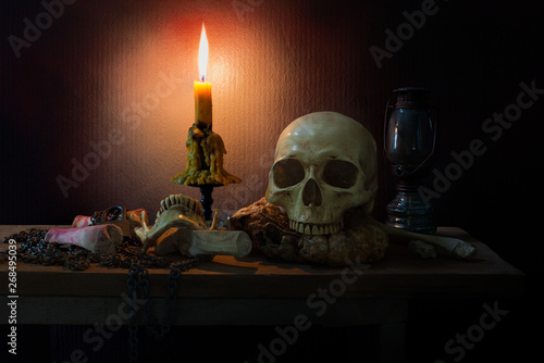 Skull on rotten pumpkin with candle light and lantern on the plank and pile of bones and wooden wall is texture background in dark room