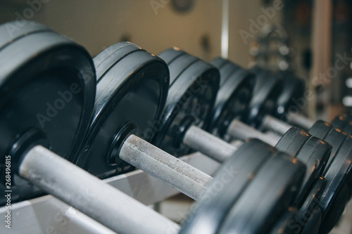 hand metal dumbbells lie together in a row on the rack in the gym close-up. training tools