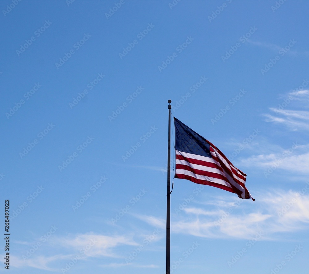 The united states flag flying in the wind with blue skies.