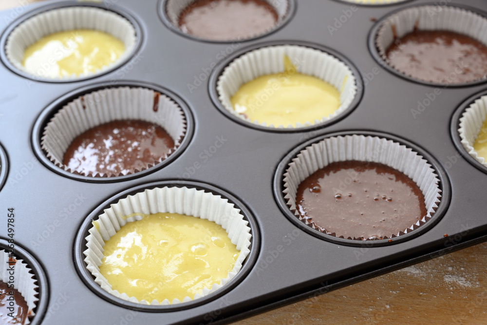 muffin baking tray filled with two kinds of cake dough, light and chocolate for delicious cupcakes muffin baking tray filled with two kinds of cake dough, light and chocolate for delicious cupcakes
