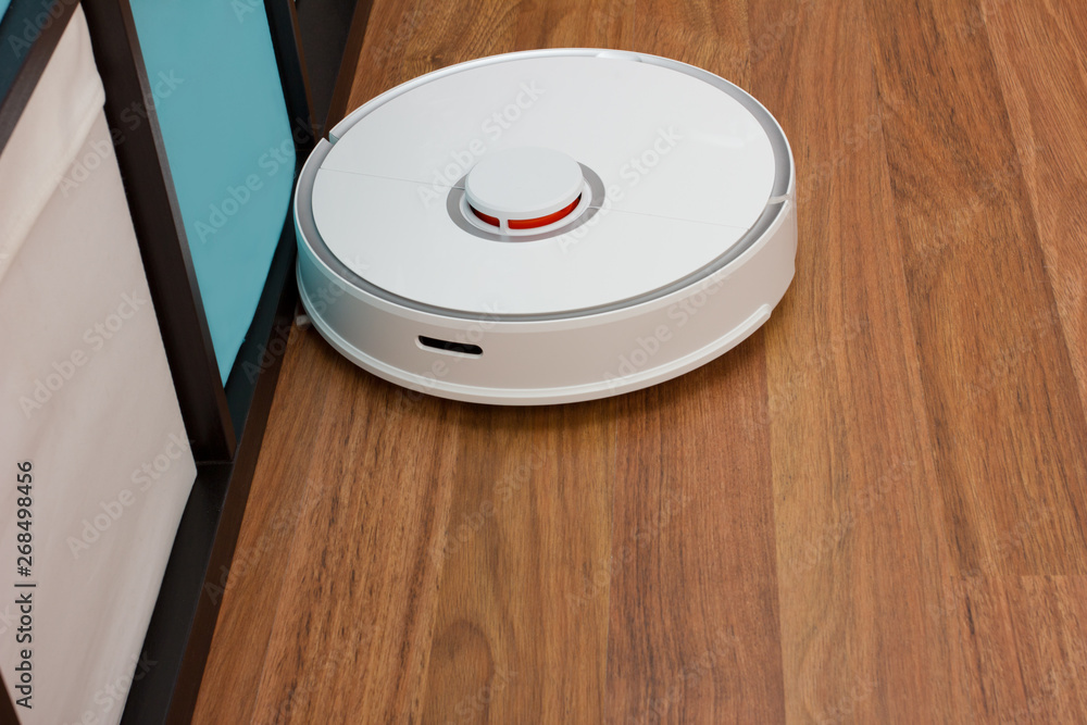 Automation cleaning. White robot vacuum cleaner collects dust, hair, washes the floor at home Automation cleaning. White robot vacuum cleaner collects dust, hair, washes the floor at home