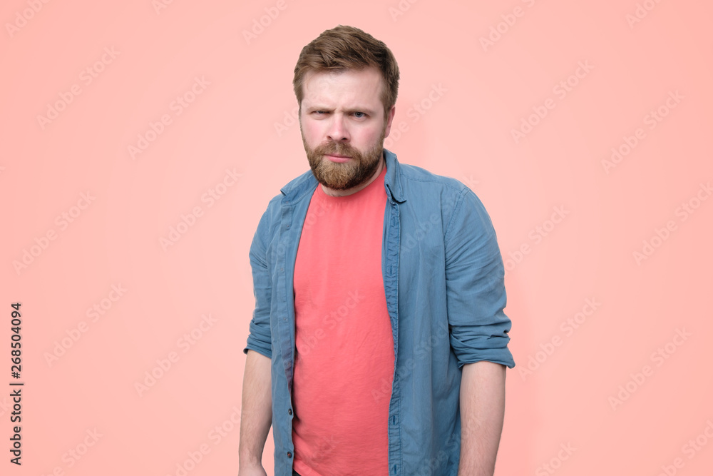 A serious, suspicious man with a frowning, intent look. Isolated on a coral background. A serious, suspicious man with a frowning, intent look. Isolated on a coral background.