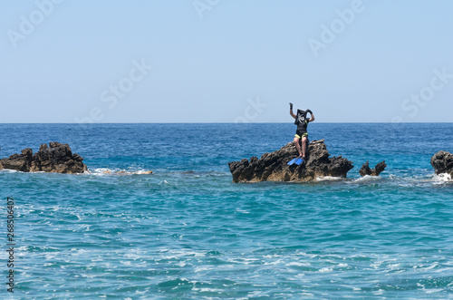 Female pirate diver captures the island in the faraway sea and announces free economic zone - a joke. Young woman, frogman, corsair with Jolly Roger flag. Seascape with human on sunny day, vacation.