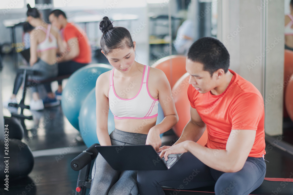 Sport women and men fitness trainer are discussing. Young Asian female talking with coach during workout with at gym. Female coach explaining with laptop computer. Sport women and men fitness trainer are discussing. Young Asian female talking with coach during workout with at gym. Female coach explaining with laptop computer.