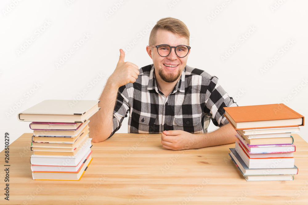 People, knowledge and education concept - smiling man sitting at the wooden table with books People, knowledge and education concept - smiling man sitting at the wooden table with books