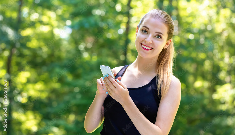 Young woman using her cellphone on a bright summer day in the forest Young woman using her cellphone on a bright summer day in the forest