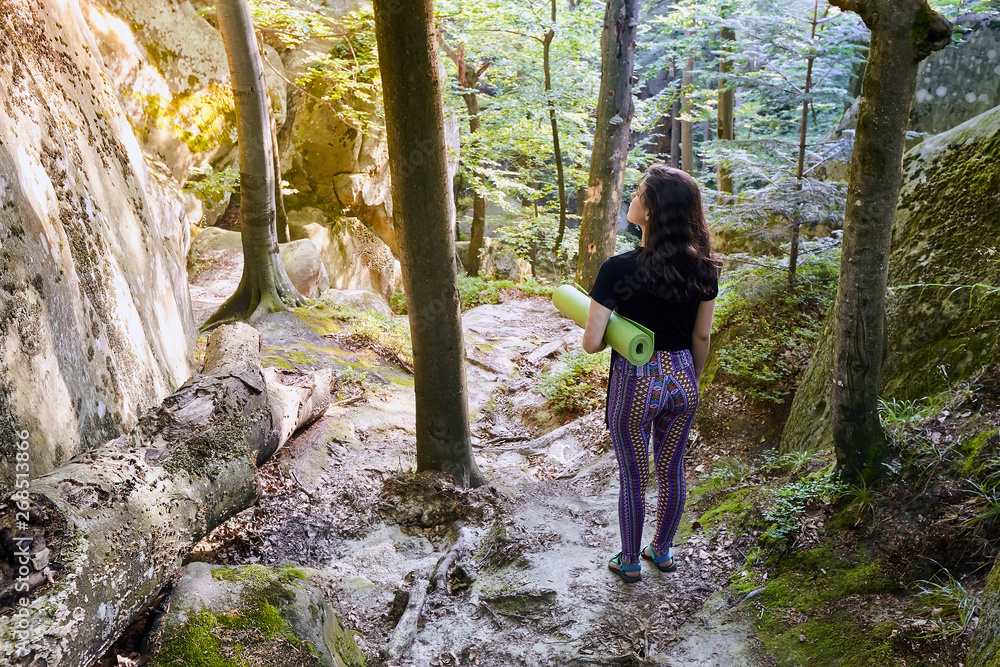 Young attractive girl in the mountain forest in sun light is holding a yoga mat Young attractive girl in the mountain forest in sun light is holding a yoga mat