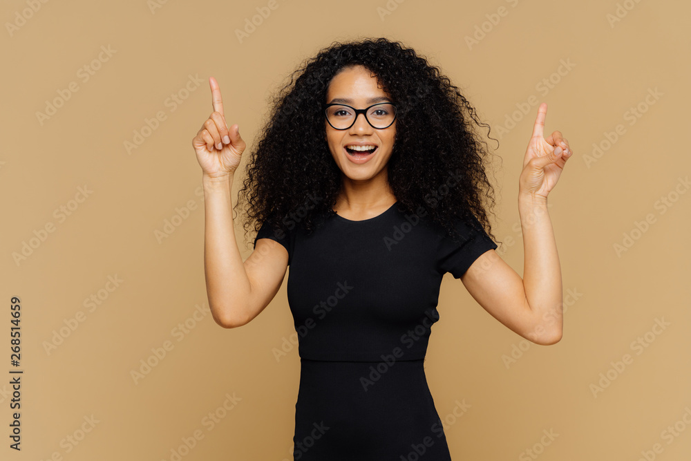 Look upwards. Happy African American woman points above with both index ...