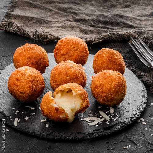 Fried potato cheese balls or croquettes with spices on black plate over dark stone background. Unhealthy food, top view photo