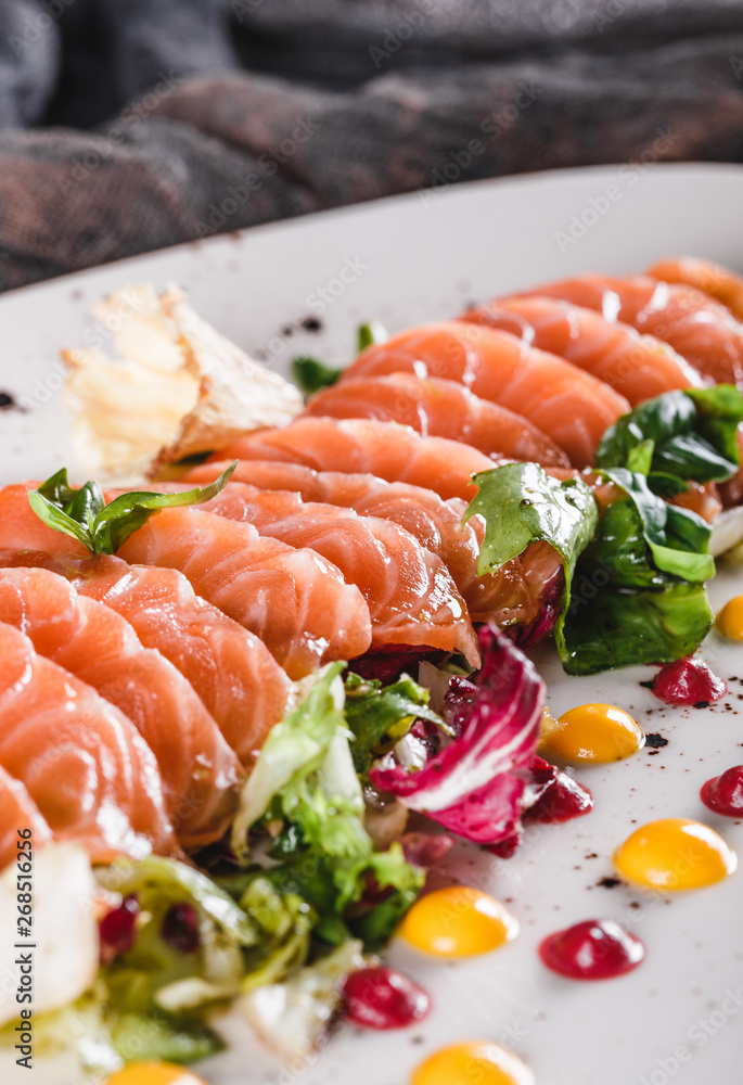 Salad of sliced salmon fillet with lettuce, cabbage and sauce in plate on dark grey background. Healthy food, clean eating, dieting, closeup Salad of sliced salmon fillet with lettuce, cabbage and sauce in plate on dark grey background. Healthy food, clean eating, dieting, closeup