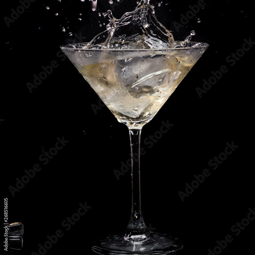 in a martini glass  vermouth ice falls  and splashes with drops on a black background