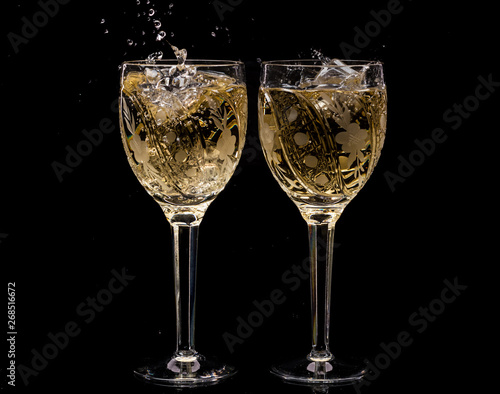 Two crystal wine glasses with a drink, falling ice and splashes