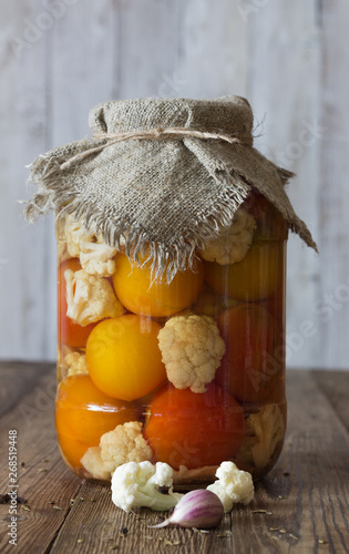 Fermented tomatoes and cauliflower in a glass jar on a natural white background. Close up. Rustic stylle photo