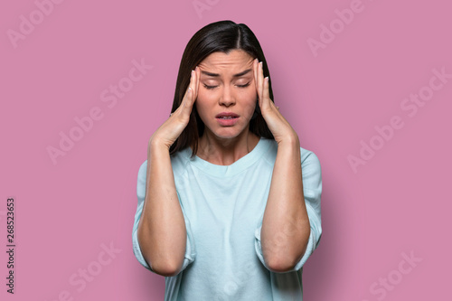 Woman overwhelmed with stress and concern, confusion and doubt, hands to head, on pink background photo
