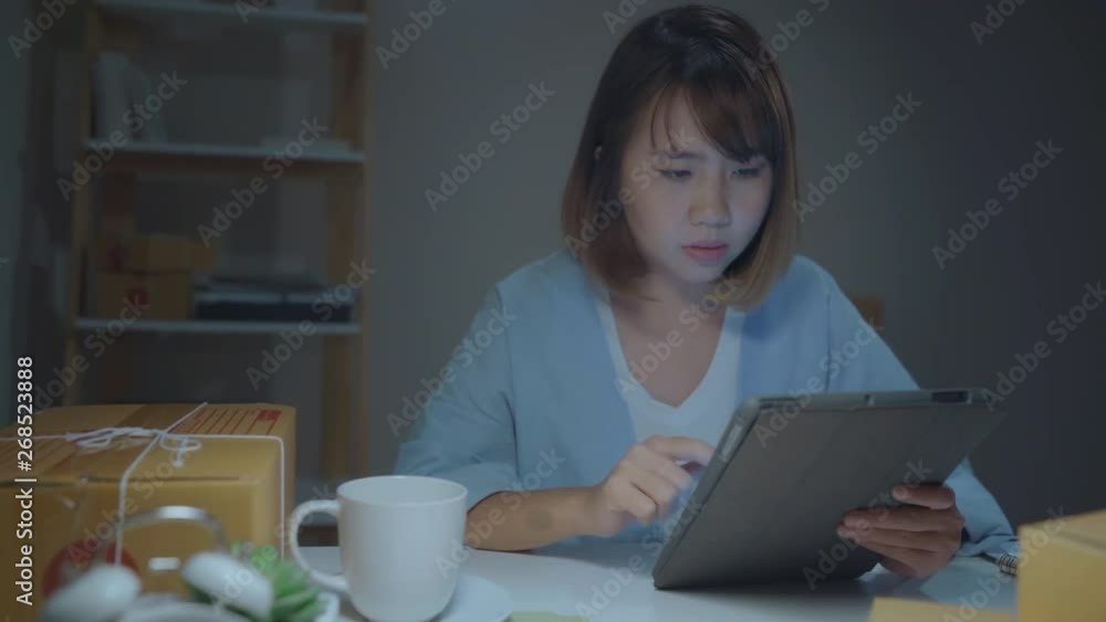 Asian young entrepreneur business woman owner of SME online checking product on stock and save to tablet and drinking coffee working late in night at home. Small business owner at home office concept. Asian young entrepreneur business woman owner of SME online checking product on stock and save to tablet and drinking coffee working late in night at home. Small business owner at home office concept.