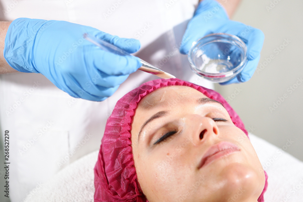 Naklejka premium A cosmetologist puts a remedy on the face for the patient to nourish, moisturize and rejuvenate the skin. Cosmetology procedure in cosmetology clinic.